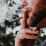 Man smoking a rolled cigarette; smoke is exhaling.