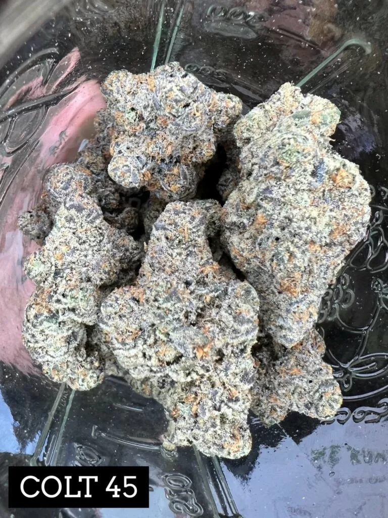 Several cannabis buds in a glass jar. The buds are gray, green, and purple, and the words 