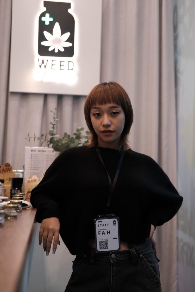 Woman with short brown hair, wearing a black sweater and jeans, stands behind a counter with a 