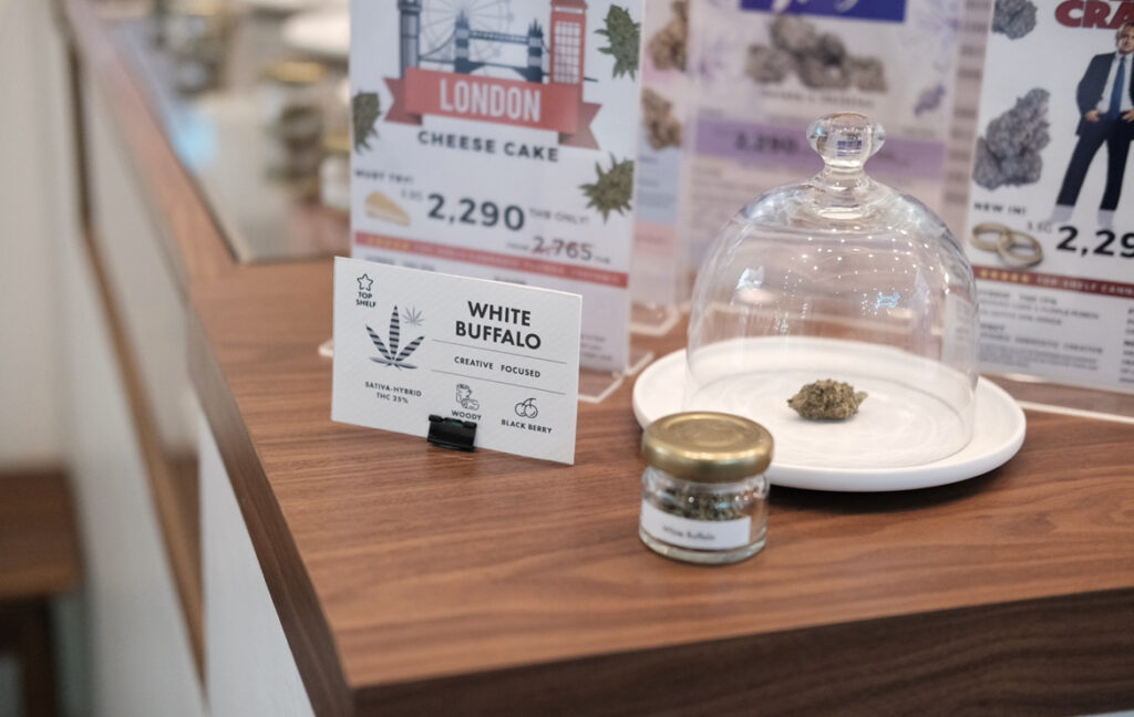 A display of cannabis products, including a bud under a glass dome, a small jar, and information cards with the labels 