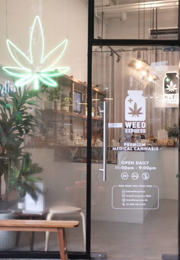 Green neon cannabis leaf sign above a glass door with 