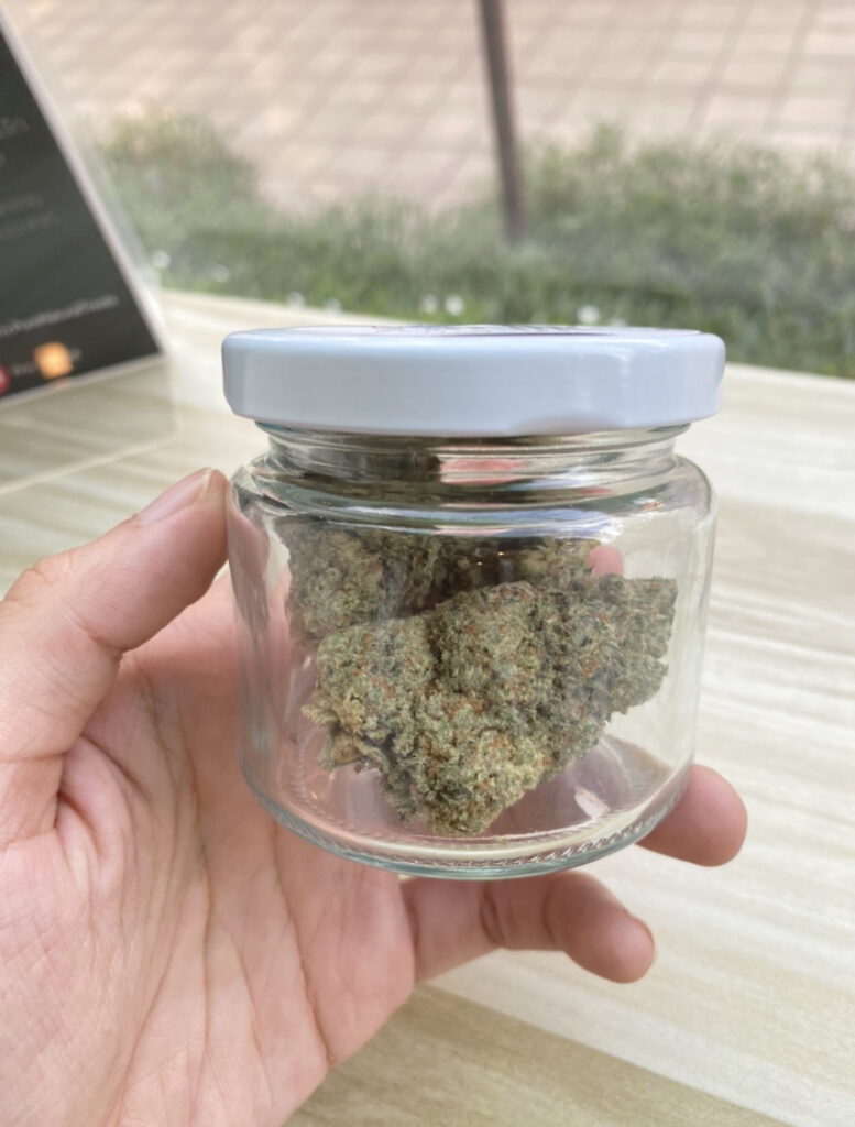 Hand holding a glass jar with white lid containing cannabis buds.