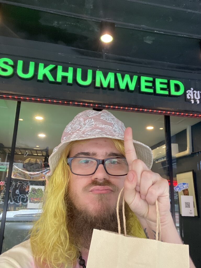 Man with blonde hair, glasses, and hat holding up a finger in front of a 
