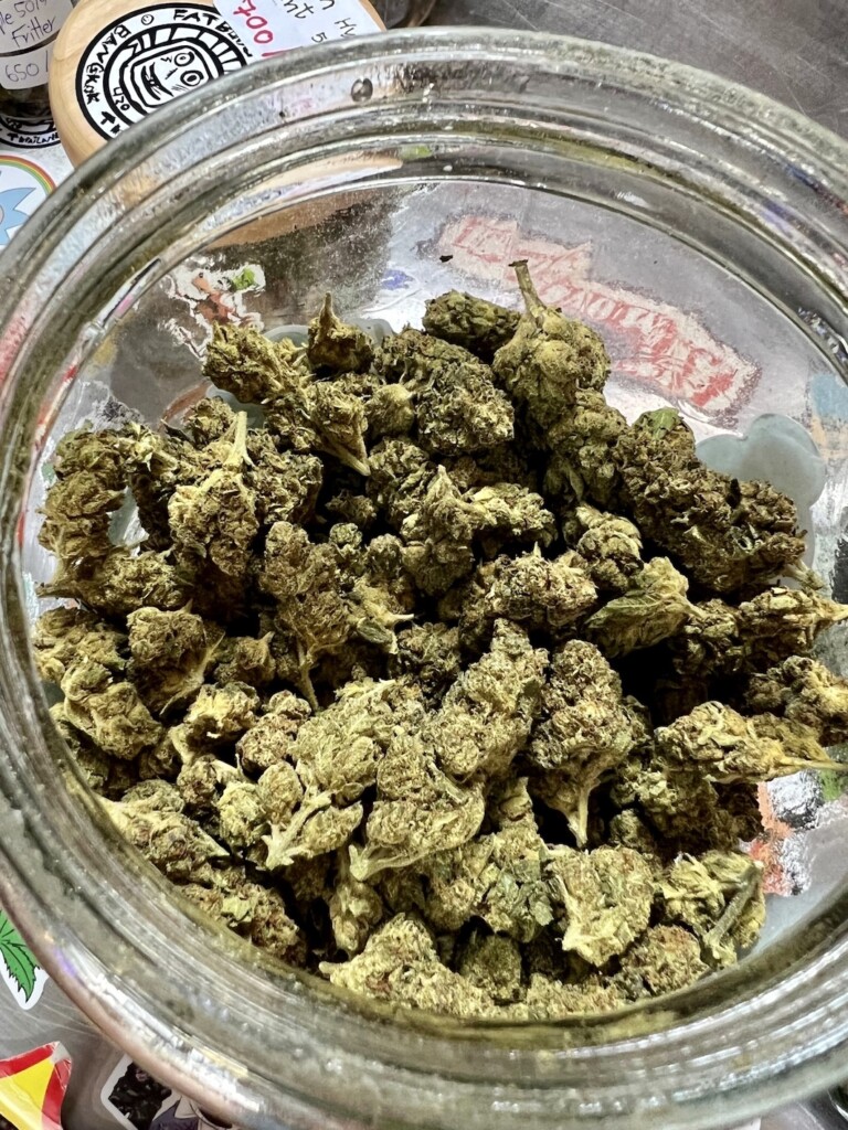 Jar of green cannabis buds viewed from above.