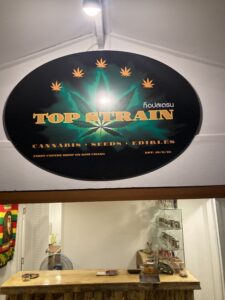 Sign for Top Strain cannabis shop on Koh Chang with text and a cannabis leaf graphic above a counter.