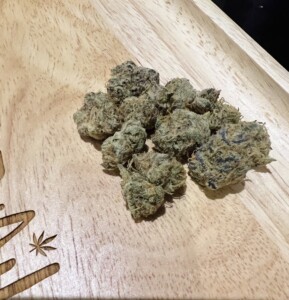 Pile of cannabis buds on a wooden tray with a leaf design.