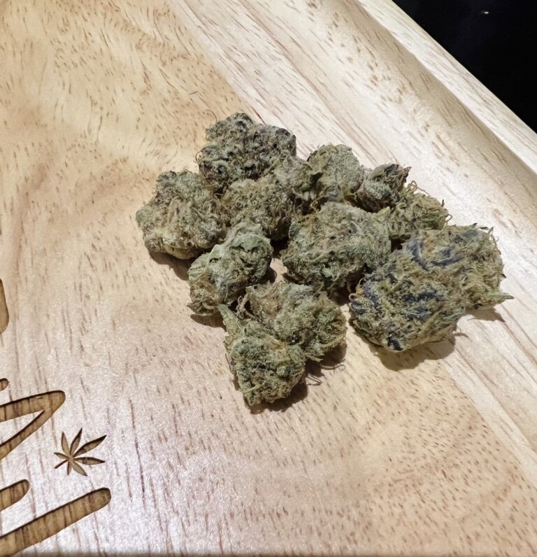 Pile of cannabis buds on a wooden tray with a leaf design.