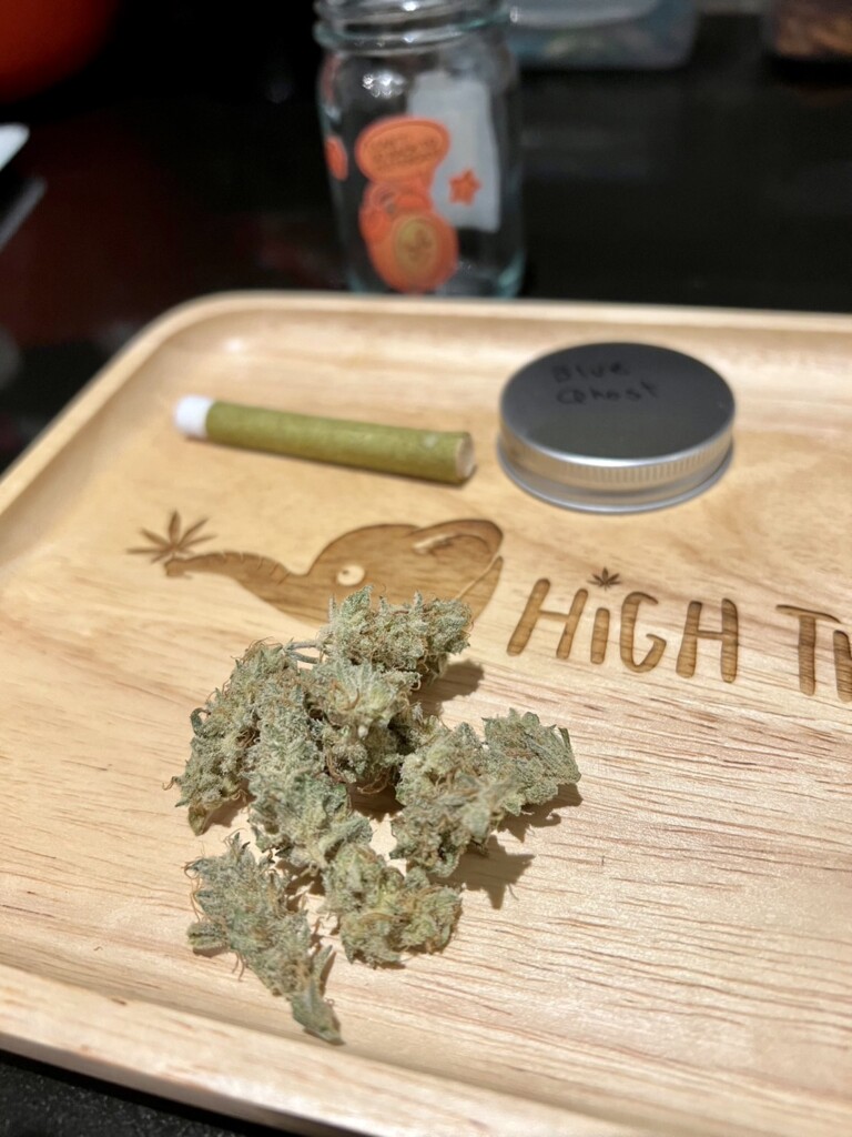 Cannabis buds on a wooden tray with a pre-rolled joint, a lid labeled 