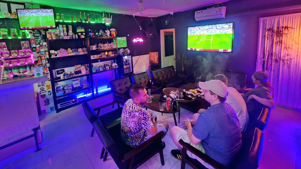 Four men watching a soccer game on TV in a dimly lit room, surrounded by shelves of products.