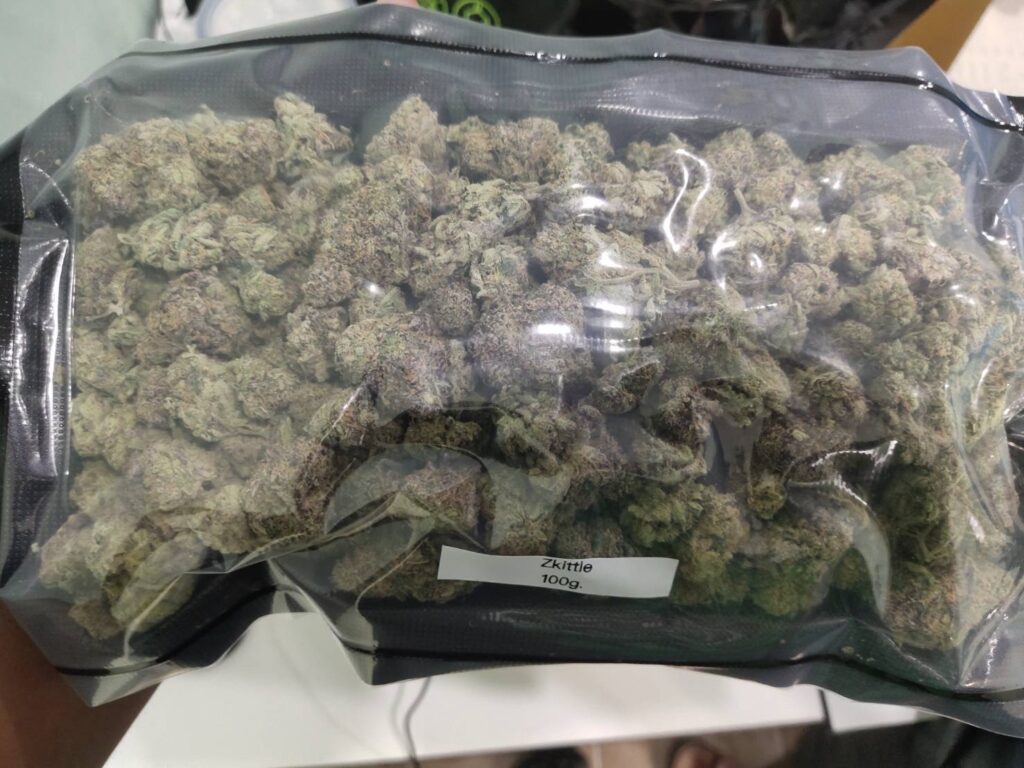 A clear plastic bag filled with green and purple cannabis buds, labeled 