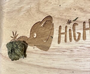 Carved wooden tray with a cannabis bud near a carved elephant head, the word 