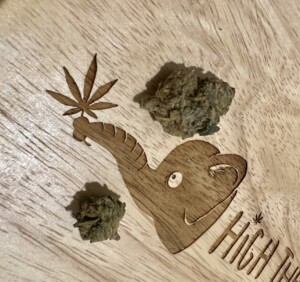 Wooden carving of an elephant, with two cannabis buds and a carved cannabis leaf.