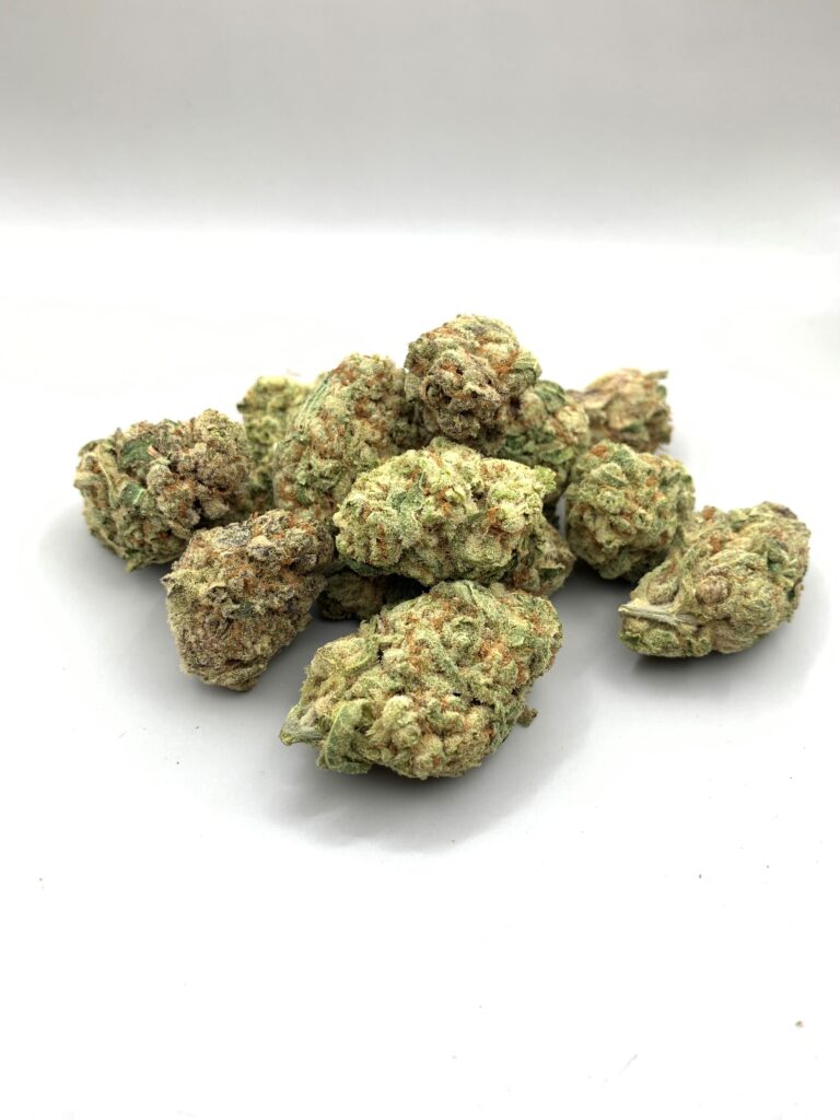 Pile of cannabis buds, with green, tan, and orange tones, on a white surface.