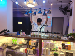Interior of High Again dispensary in Ram Inthra, Bangkok, showing cannabis products and staff with arms raised.