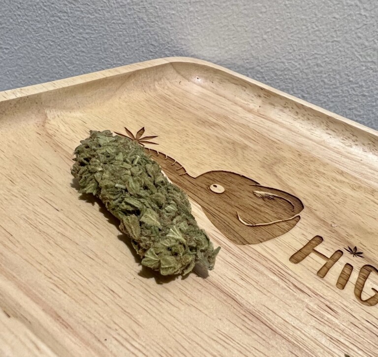 Cannabis bud on a wooden tray engraved with a whale-like creature and the word 