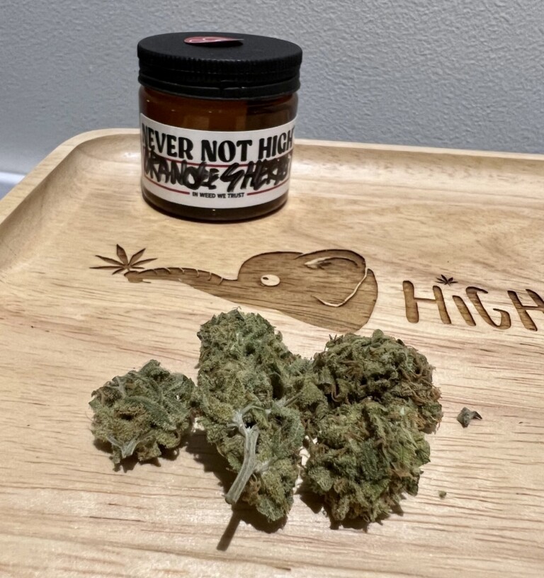 Three cannabis buds on a wooden tray with a jar labeled 