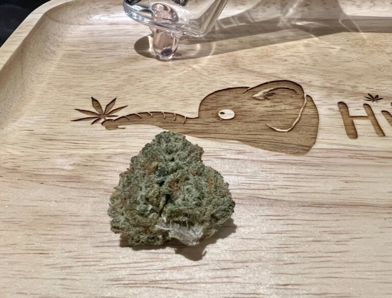 Cannabis bud on wooden tray with etched elephant design and leaf graphic.