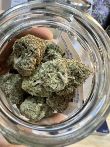 Green cannabis buds inside a clear glass jar.