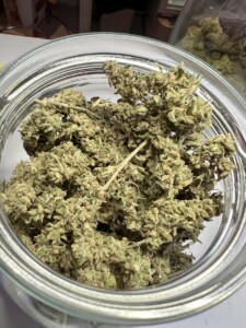 Green cannabis buds inside a clear glass jar.