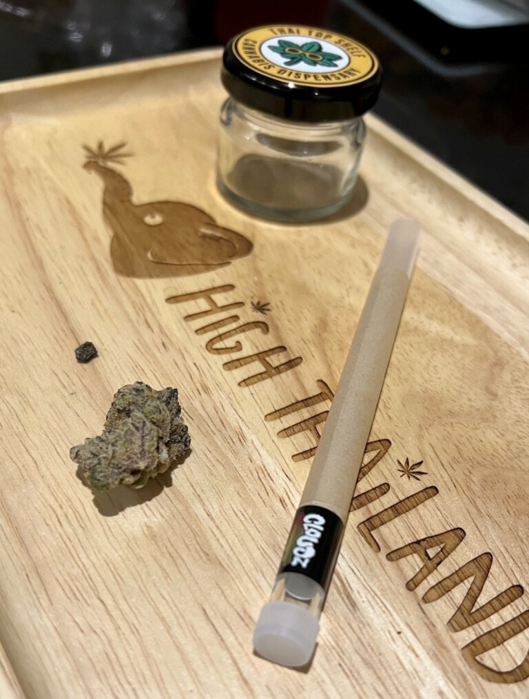Wooden tray with pre-rolled joint, cannabis bud, and small jar labeled 