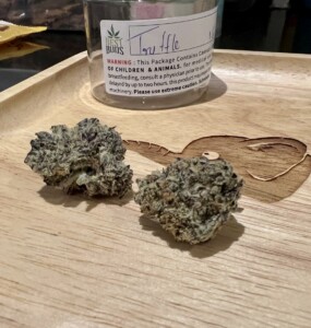 Two cannabis buds, one with a Best Buds label, on a wooden tray.