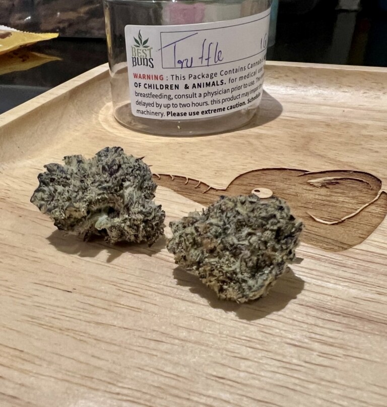 Two cannabis buds, one with a Best Buds label, on a wooden tray.