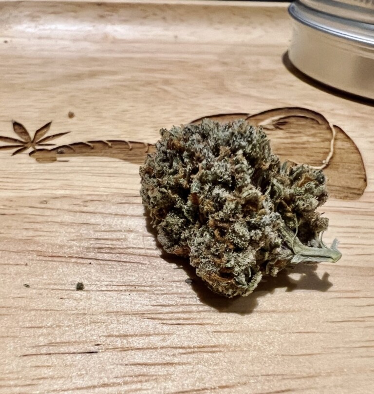 A cannabis bud rests on a wooden tray with a carved marijuana leaf.