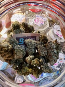 Green cannabis buds inside a clear glass jar with a label showing 