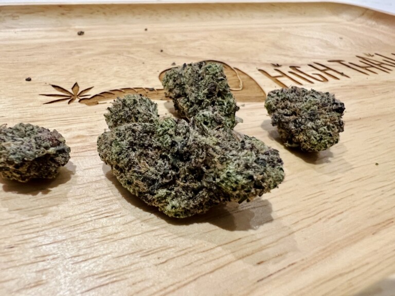 Four cannabis buds on a wooden tray with a marijuana leaf carving.