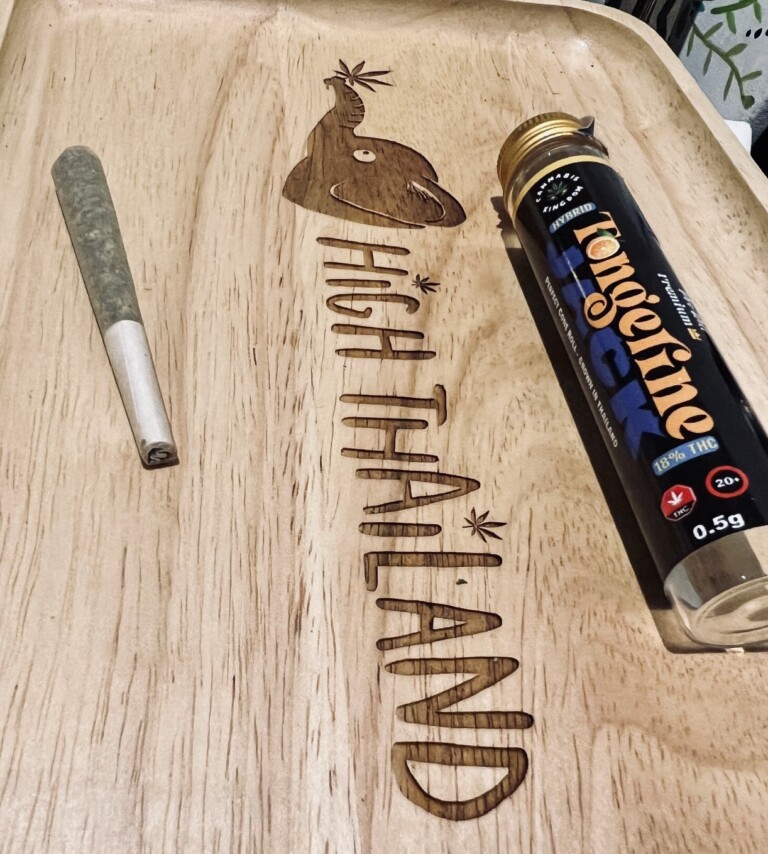 Cannabis joint and 'Tangerine' pre-roll tube on a wooden tray with 'High Thailand' engraving.