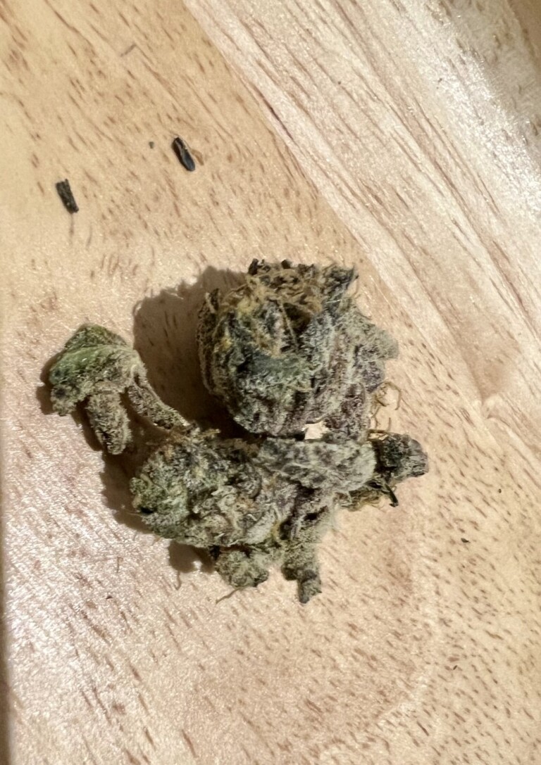 Three cannabis flower buds on a wooden surface.
