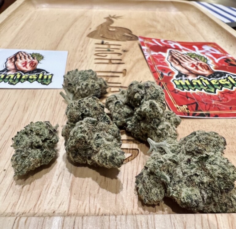 Cannabis flower buds on a wooden tray with branded stickers.