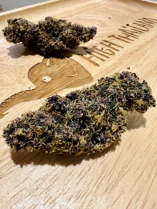 Two purple cannabis nugs on a wooden tray.