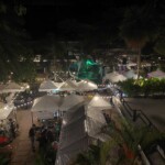 Night market scene with white tents and string lights, viewed from above.