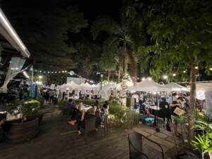 Night market with people, vendor tents, string lights, and outdoor seating.