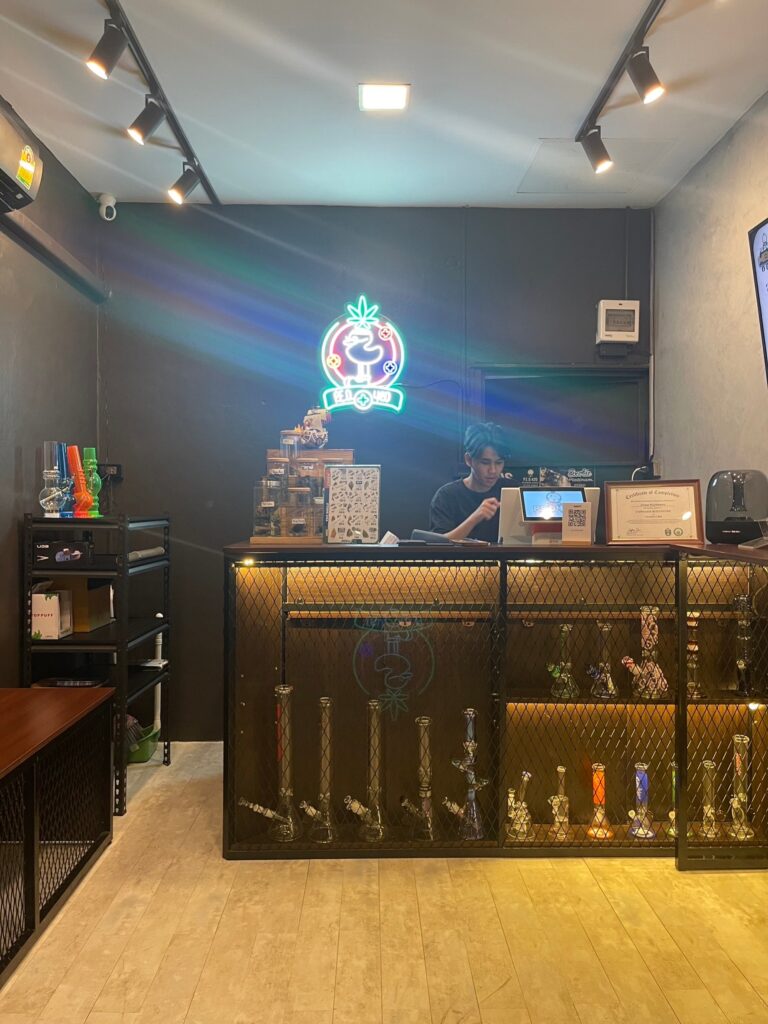 Cannabis dispensary interior with clerk at counter and display of bongs.
