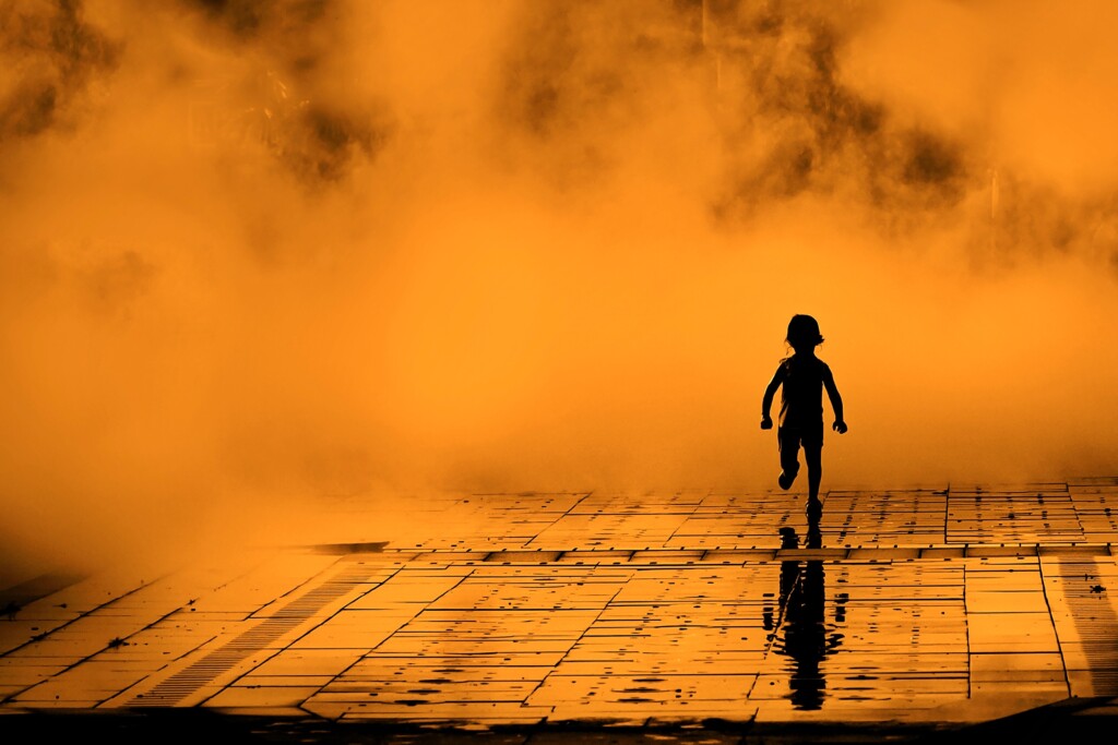 Silhouette of a child running on wet pavement, orange mist background.
