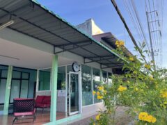 Exterior of East Side Cannabis Dispensary in Takua Pa, Phang-nga, Thailand, showing entrance with cannabis sign, open-air seating, and yellow flowers.