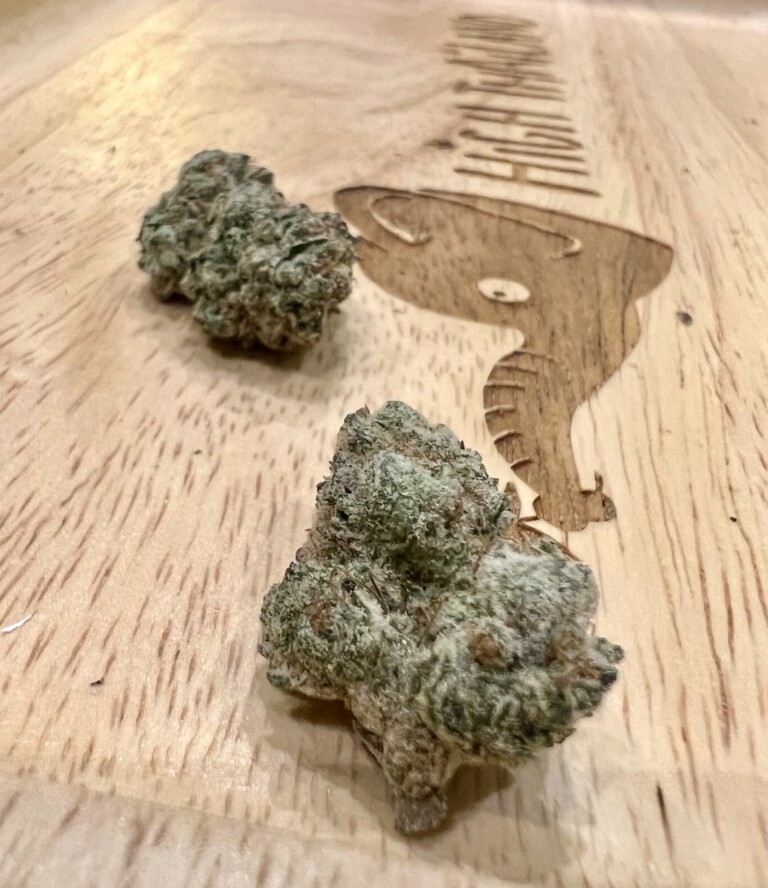 Two cannabis flower buds on a wooden tray with a logo.