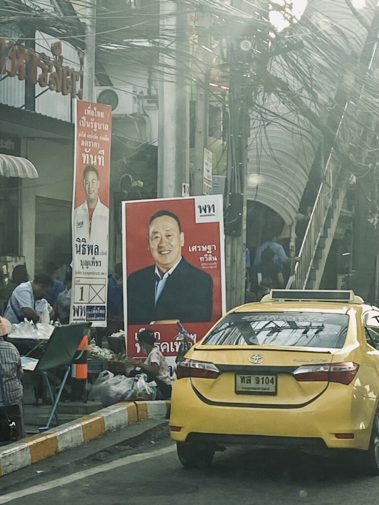 Bangkok street scene with political posters and a yellow taxi.