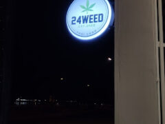 Illuminated sign of 24WEED cannabis shop in Sri Chiang Mai, Thailand, displaying a cannabis leaf.