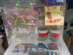 6 TON dispensary display case in Thung Pho, Uthai Thani, Thailand. Cannabis flowers, Wedding Cake strain, and smoking accessories visible.