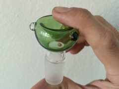 Green glass cannabis bowl held in hand, smoking accessories for sale.