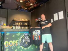 Interior of Dope Dealer cannabis shop in Koh Chang, Thailand, with shelves of flower and staff holding branded t-shirt.