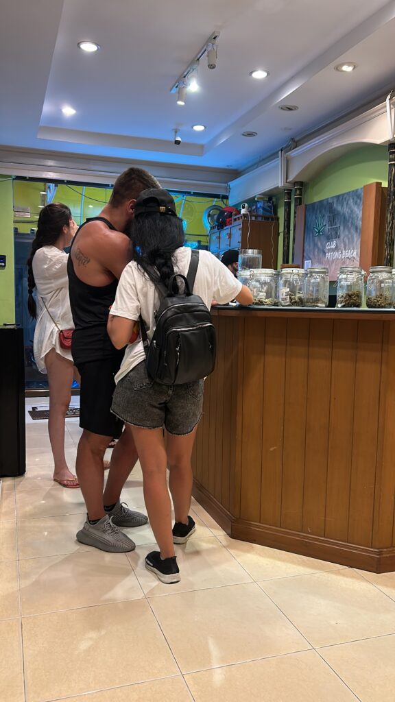 People at a cannabis dispensary counter with jars of cannabis.