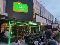 Exterior of KING CANNABIS dispensary in Pattaya City, Thailand, with neon signage and people gathered outside.