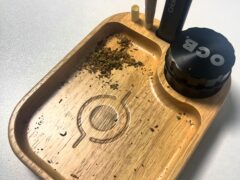Wooden rolling tray with a pre-roll, lighter, OCB grinder, and cannabis flower.