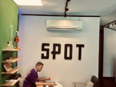 Man sitting at a table inside SPOT, cannabis cafe in Bangkok, with bong and smoking accessories visible.