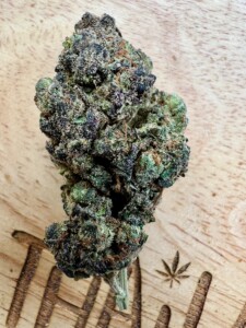 Close-up of a green and purple cannabis bud on a wooden surface.