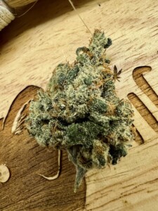 Close-up of a green cannabis flower bud on a wooden surface.